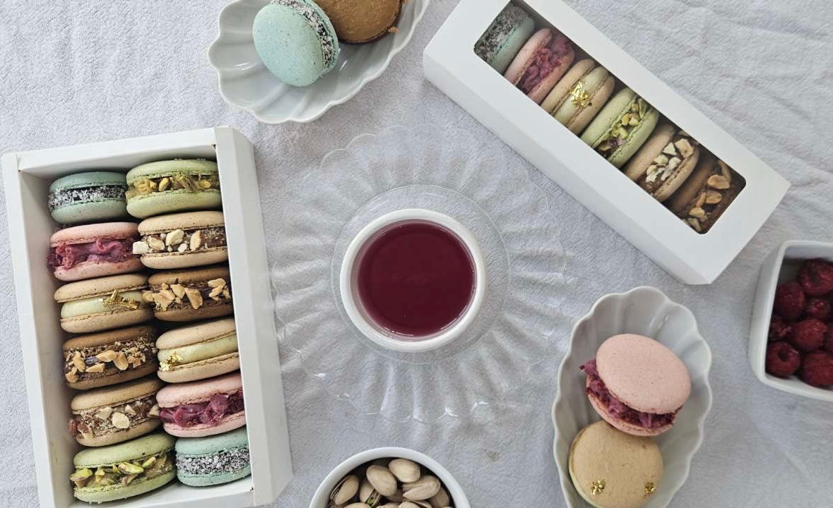Table élégante avec deux box de macarons artisanaux assortis, accompagnées de macarons individuels, pistaches, framboises et une thé fruité en centre